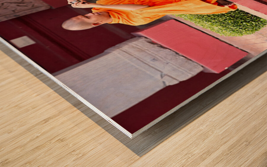 Monk in orange robes takes photo by a lotus pond. Wood print