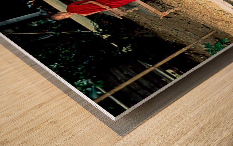 Young monk stands by water in Myanmar during daytime Wood print