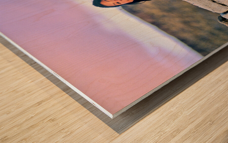 Young girl smiles over stone wall at sunset. Wood print