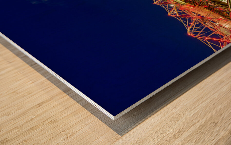 People walk across the Helix Bridge as the Marina Bay Sands Hotel shines at sunset. The sky turns orange and lights reflect in the water. Wood print