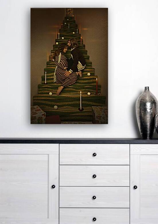 Vintage scene of a man and a pregnant woman from the 1970s sitting in a staircase creating the illusion of a Christmas tree loving each other surrounded by candles ornaments and gifts by Artmood Visualz