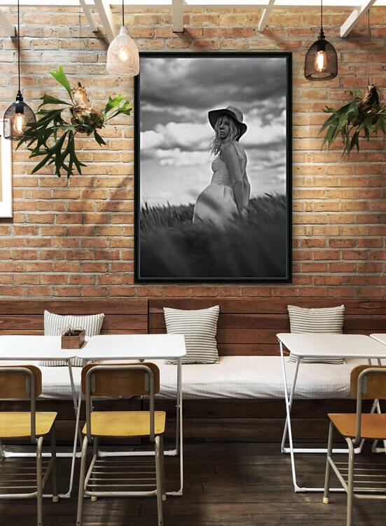Black and white portrait of a beautiful young woman wearing a summer dress and a sun hat standing outdoors in a wheat field on a cloudy day by Artmood Visualz