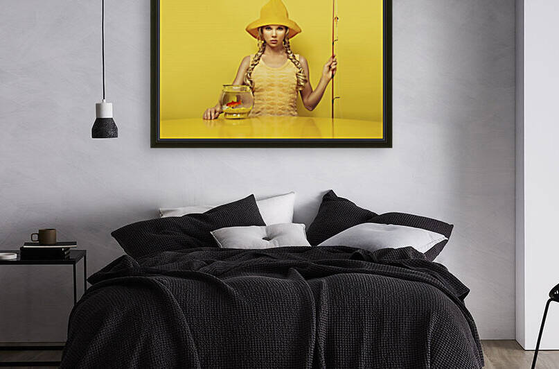 Portrait of a young fisherwoman looking at the camera dressed in a yellow dress with a fish pattern fishing a goldfish in its fishbowl placed on a yellow table by Artmood Visualz