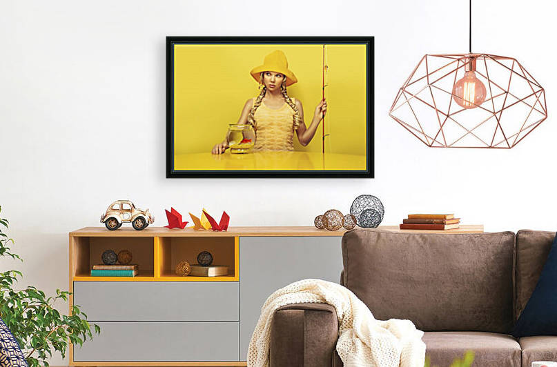 Portrait of a young fisherwoman  patiently waiting dressed in a yellow dress with a fish pattern fishing a goldfish in its fishbowl placed on a yellow table sitting in front of a yellow background by Artmood Visualz