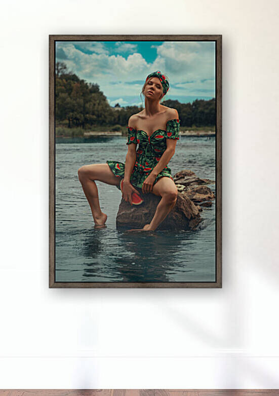 Young attractive blonde woman wearing a green summer outfit with a watermelon pattern holding a piece of watermelon while sitting on a rock in the middle of a river on a sunny day by Artmood Visualz