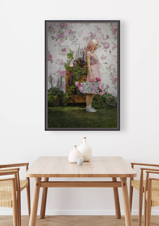 Young woman with light pink hair standing in front of a dresser full of plants holding a suitcase overflowing with flowers by Artmood Visualz