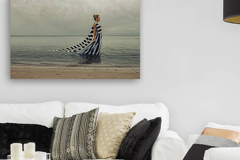 Beautiful young blonde woman wearing a long white and blue striped summer dress walking in the water of the sea by the beach shore under a cloudy sky by Artmood Visualz