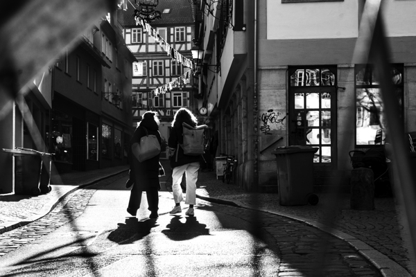 Black and white street photo of people walking down the road seen through the spokes of a bicycle Digital Download