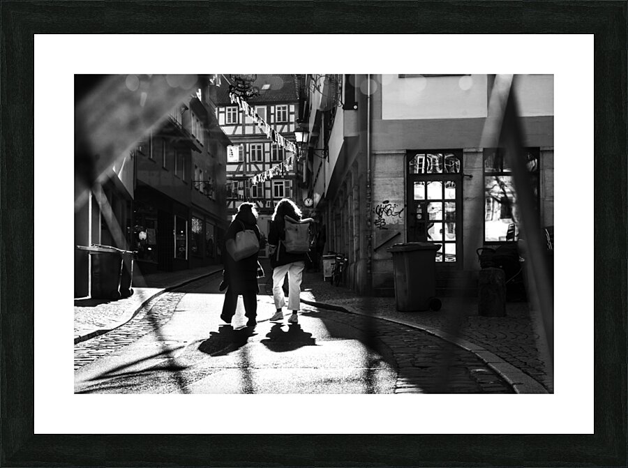 Black and white street photo of people walking down the road seen through the spokes of a bicycle Picture Frame print