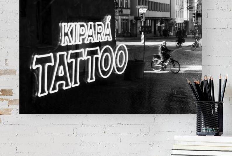 Black and white capture of the mirror image of people on bicycles in the window of a tattoo studio   by caladoart
