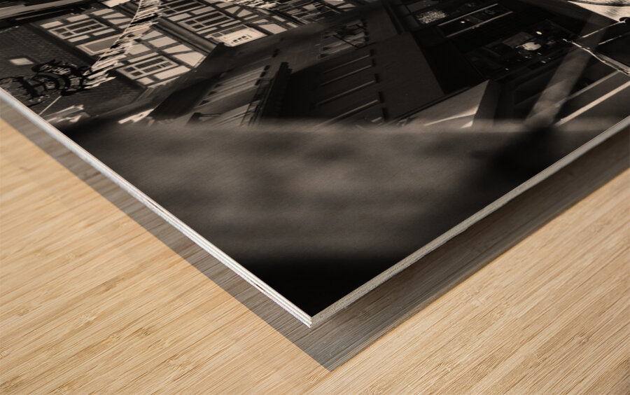 Black and white street photo of people walking down the road seen through the spokes of a bicycle Wood print