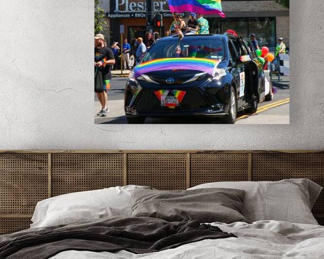 Large rainbow flag sticking out of a car durning by Woodys Photos