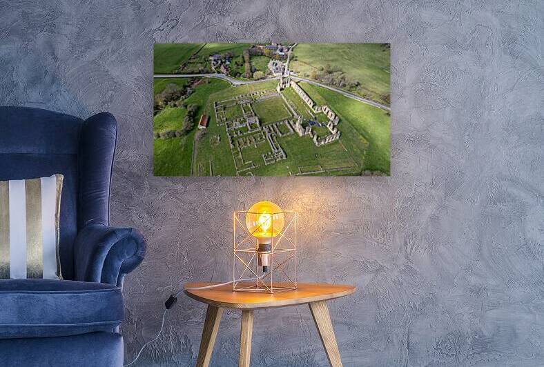 Aerial view of ancient abbey ruins in lush green landscape with adjacent road. by Vasile Jechiu