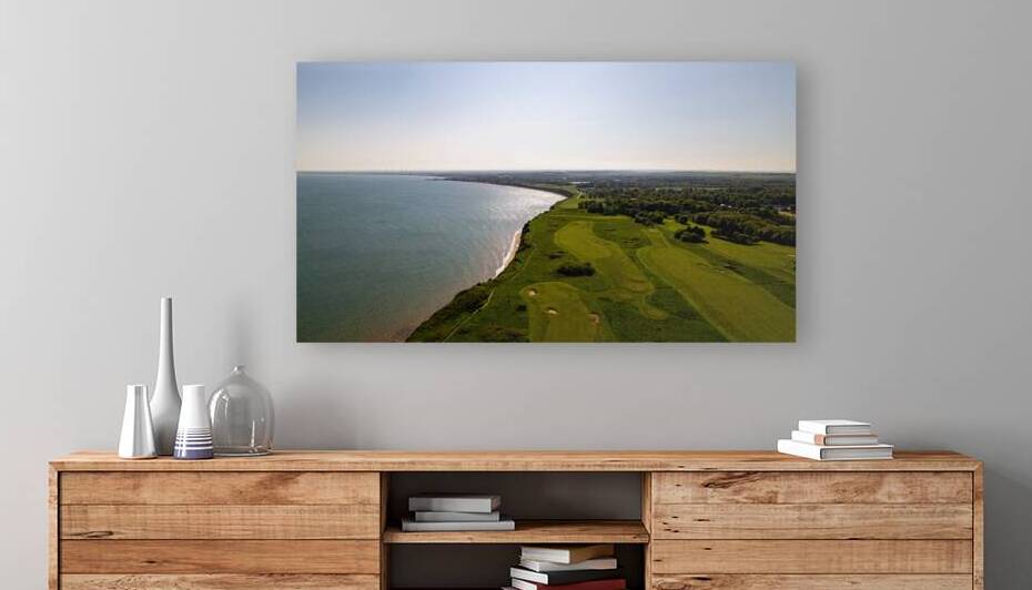 Aerial view of a coastal golf course with lush green fairways next to a calm sea under a clear sky in Flamborough England by Vasile Jechiu