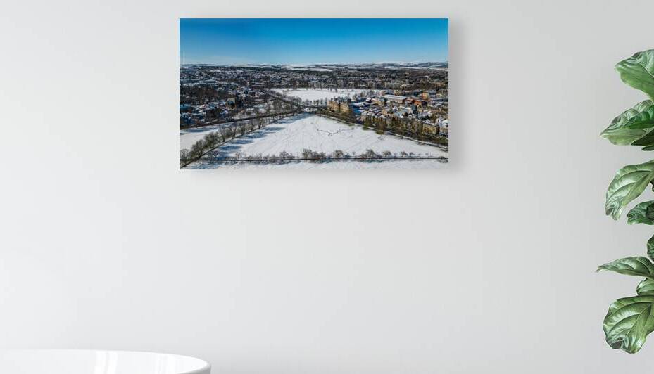 Aerial winter view of a snow-covered town with buildings and bare trees under a clear blue sky in Harrogate North Yorkshire. by Vasile Jechiu