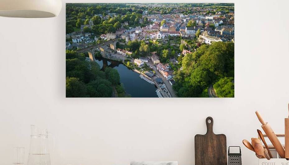 Aerial view of a quaint European town with historic buildings along a river lush greenery and a bridge Aerial view of a historic town with an ancient tower surrounded by lush green trees under a clear blue sky in Knaresborough North Yorkshire. by Vasile Jechiu